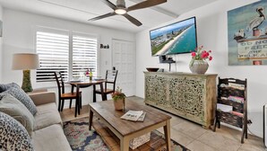 A living room with a ceiling fan, a television, a dining area with a table and chairs, a sofa, and a cabinet with decorative carvings. - Beach Steps Away: Garden Oasis with Pool & Jacuzzi (South Padre Island)