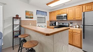 Una cocina moderna con armarios de madera, un refrigerador de acero inoxidable, un microondas, una estufa y una zona de bar con taburetes.