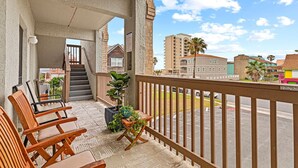 Un balcón con sillas de madera, una planta en maceta y vista de un paisaje urbano con edificios y una palmera.