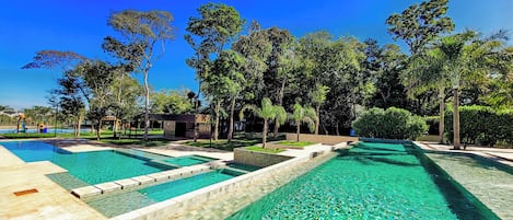 A swimming pool area with multiple pools, surrounded by trees and a small building.