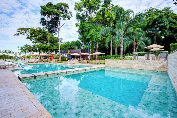 A swimming pool with lounge chairs and umbrellas, surrounded by trees and a stone wall. - Doubletree by Hilton Foz do Iguacu (Foz do Iguaçu)