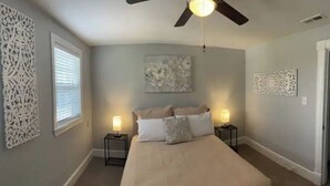 Ein Schlafzimmer mit einem Bett, zwei Nachttischen, einem Deckenventilator und Wanddekoration.