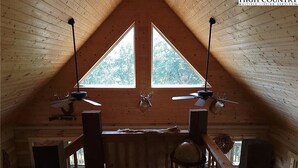 A wooden attic room with two windows, a ceiling fan, and a table.
