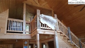 A wooden cabin interior with a kitchen, a dining area, and a staircase.