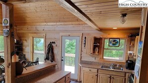 A wooden cabin with a kitchen featuring wooden cabinets, granite countertops, and a large window.