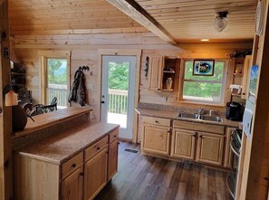 Une cabane en bois dotée d’une cuisine avec des meubles en bois, des comptoirs en granit et une grande fenêtre.