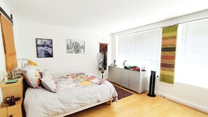 A bedroom with a bed, a radiator, a wardrobe, and a window with blinds.