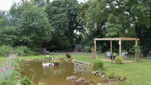 A garden with a pond, a wooden pergola, and potted plants.