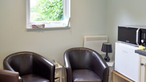A small room with two leather chairs, a white radiator, a microwave, and a window with a view of greenery.