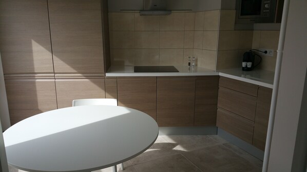 A compact kitchen with a white countertop, wooden cabinets, and a white table.