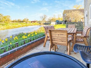 A patio with a table and chairs, a grill, and a view of a canal with yellow flowers.