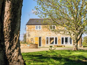 A stone house with a large window, a door, and a small tree in the front yard.