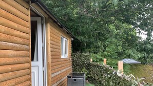 Una cabana de fusta amb una porta oberta, una finestra i un paperer negre.