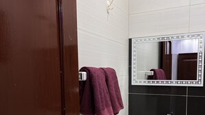 Une salle de bain avec un lavabo blanc, un miroir doté d’un cadre décoratif et une serviette violette suspendue à un porte-serviettes.