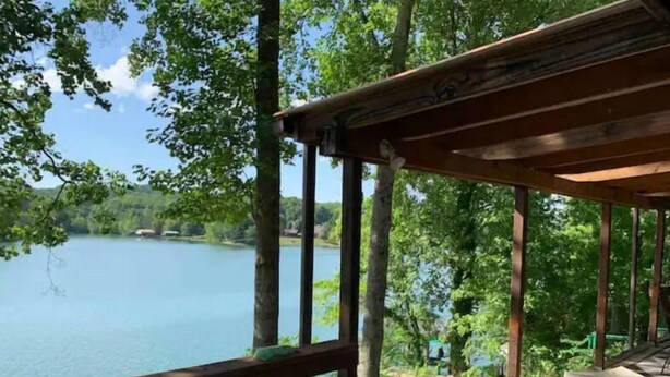 Una terraza de madera con vista a un lago, rodeada de árboles.