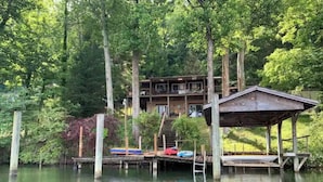 Una cabaña junto al lago con un muelle, rodeada de un bosque denso.