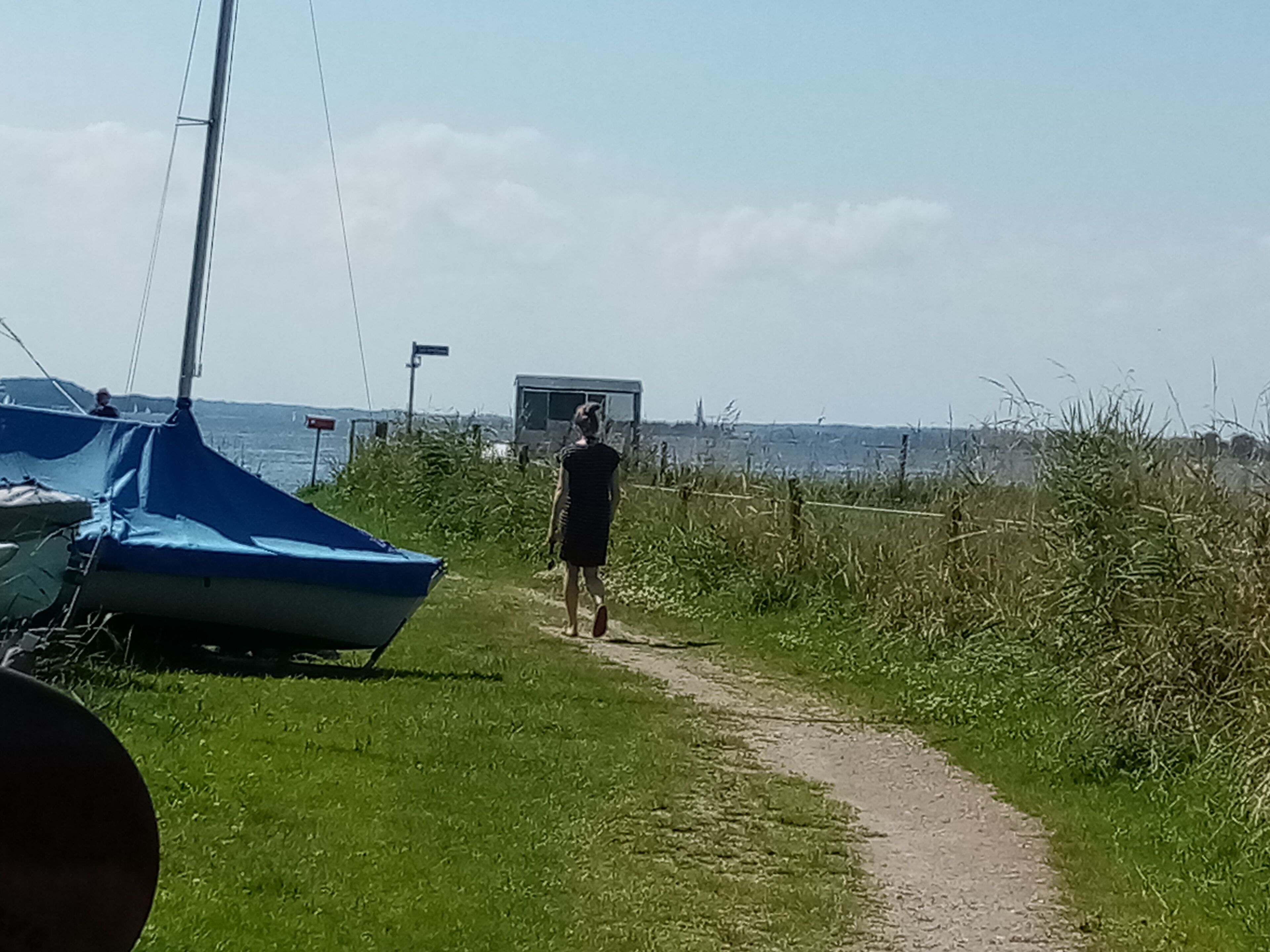 En stig som leder till en strand där det finns en segelbåt och ett släpvagn.