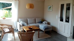 A cozy living room with a sofa, two wicker chairs, a wooden coffee table, and a hanging light fixture.