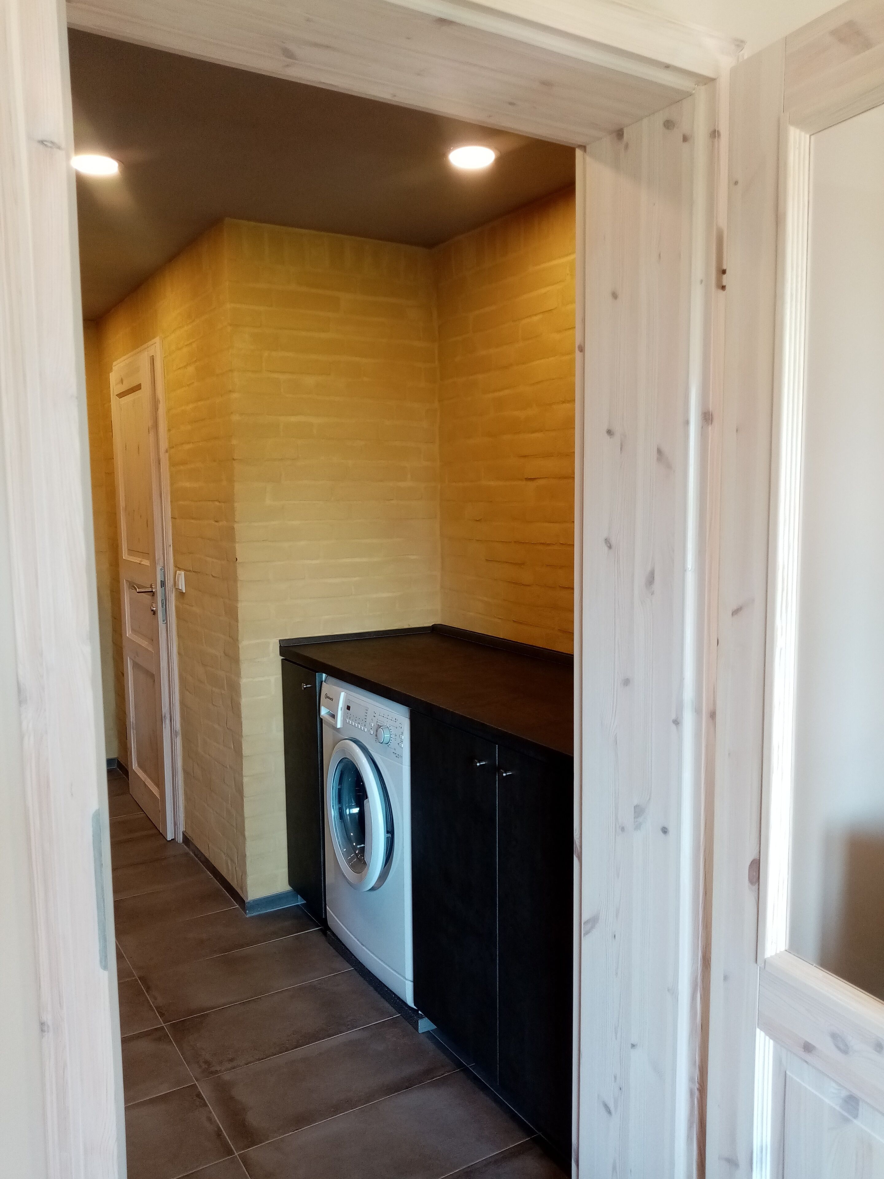 A laundry room with a washing machine, wooden walls, and a tiled floor.