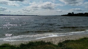 A beach with waves, a distant sailboat, and a partly cloudy sky.