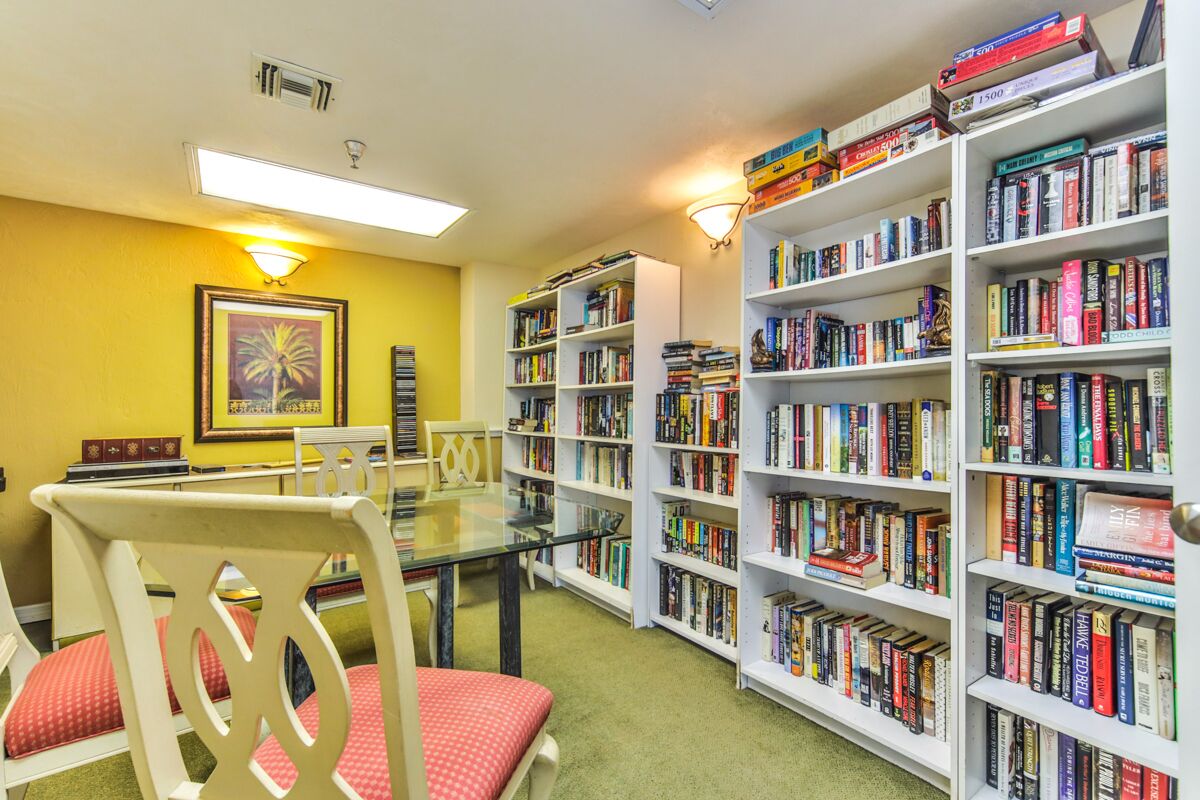 A library with white bookshelves, a glass table, and chairs.