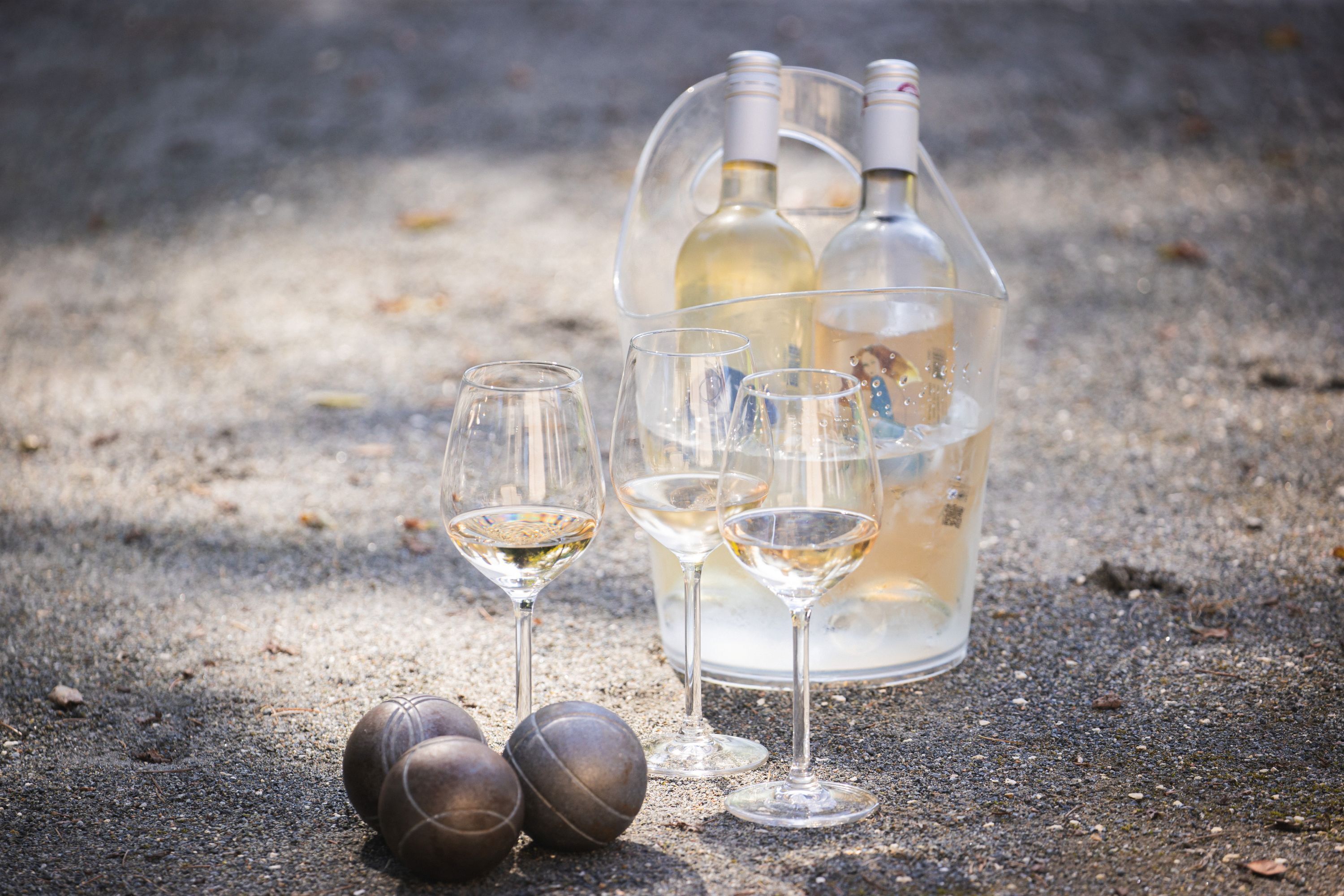 A bottle of white wine, two wine glasses, and three small balls on a textured surface.