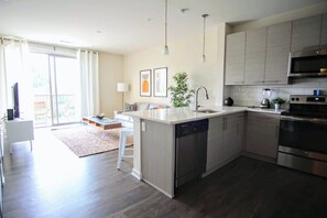 A modern kitchen with a dishwasher, stove, and microwave. There is a dining area with a table and chairs. - Top Floor Apt City Views, Fitness Center, Pool (Charlotte)