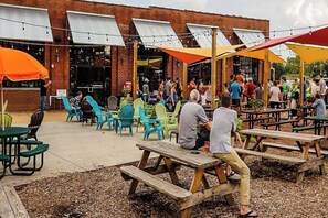 An outdoor patio area with wooden picnic tables and colorful plastic chairs, a brick building with awnings, and a crowd of people. - Pet Friendly House & Guest Studio w/ Fenced Yard (Charlotte)