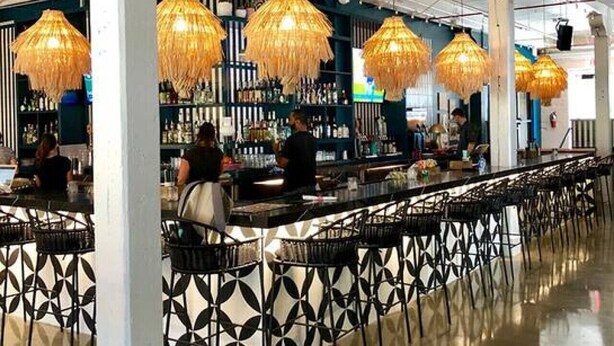 Eine moderne Bar mit hohen Decken, freiliegenden Lüftungsrohren und hängenden Korblampen.