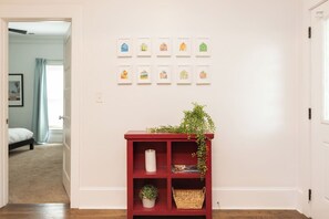 Un pasillo con una consola roja, una planta en maceta y cuadros en la pared.