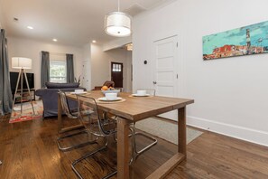 Un comedor con una mesa de madera, sillas de metal, un lámpara colgante y un cuadro en la pared.