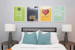 Un dormitorio con una cama, dos lámparas de noche y cuatro carteles decorativos enmarcados en la pared.
