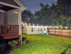 Un patio trasero con una casa, una terraza de madera y una guirnalda de luces.
