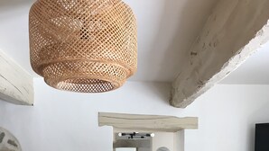 En matplats med ett träbord, stolar, en flätad hänglampa, en vas med torkade växter och en vägg av sten.