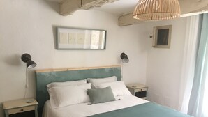 Ett sovrum med en säng, två sängbord, en väggmonterad lampa, en inramad tavla och ett fönster med gardiner.