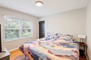A bedroom with a bed, a desk, a window with blinds, and a door. - Columbus: Cozy Cottage (Columbus)