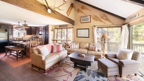 A spacious living room with a large sofa, a coffee table, and patterned chairs. There is a kitchen area with dark cabinets and a dining table. The room has wooden beams on the ceiling and large windows with curtains. - Your Four-Season Escape at Camelback Mountain
Townhouse Sleeps 10 comfortably. (Tannersville)