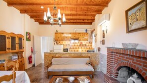 Un salon chaleureux avec un plafond en bois, une cheminée en pierre et un coin cuisine doté de meubles en bois et d’un four encastré.