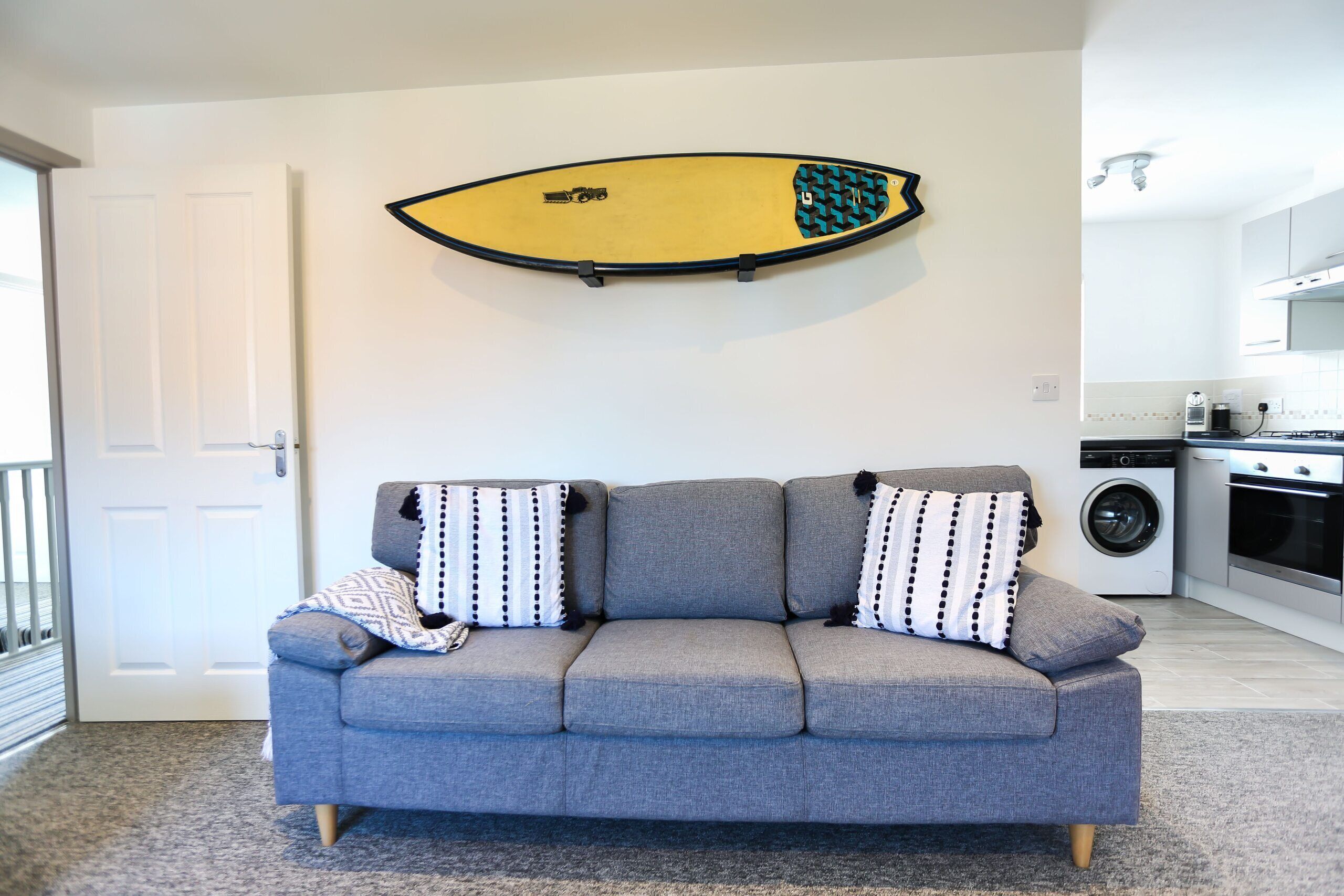 A grey sofa with patterned cushions in a living room with a surfboard mounted on the wall.