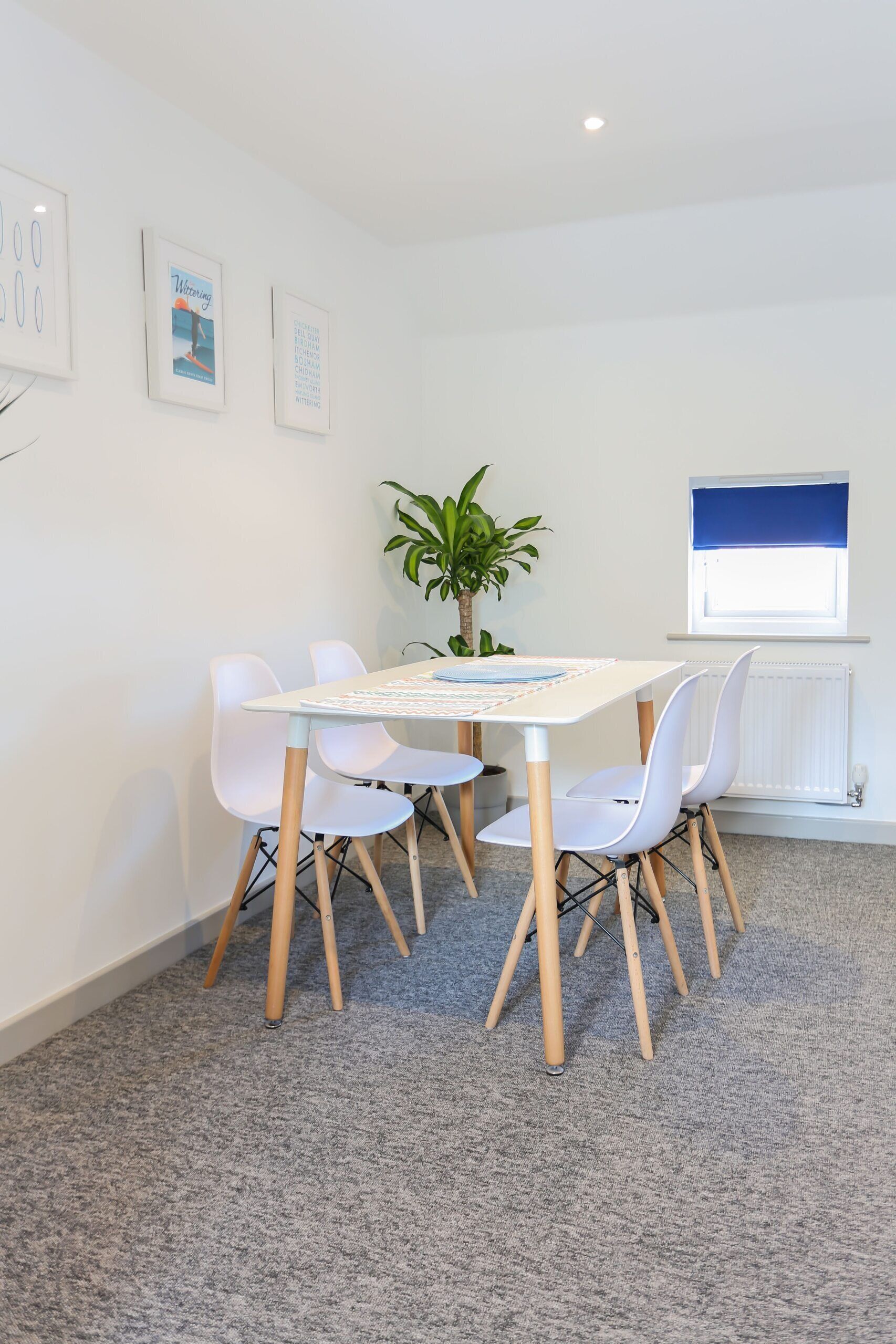 Quarto moderno com uma mesa e cadeiras brancas, uma planta em vaso e uma janela com persiana azul.