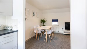 A modern kitchen with white cabinets, a countertop with jars, and a dining area with a table and chairs. - Shorebreak - Bracklesham Bay Apartment (Chichester)