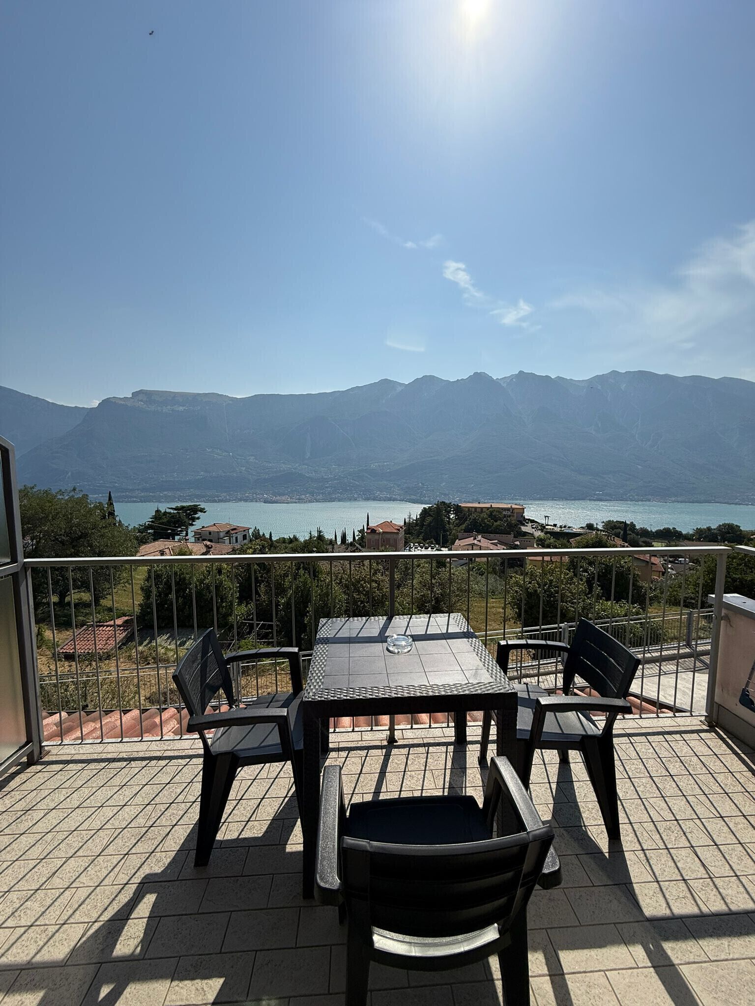 A terrace with a table and chairs, overlooking a mountainous landscape and a body of water.