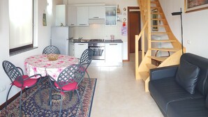 Una sala de estar acogedora con techo de madera, un comedor con mesa y sillas, una cocina con armarios blancos y una escalera de madera.