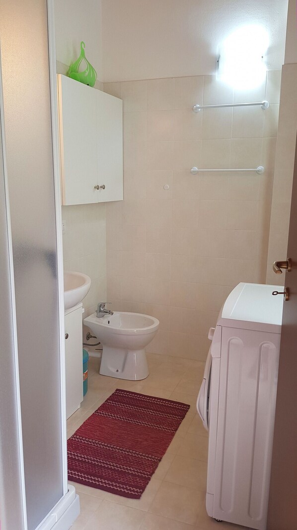 A small bathroom with a toilet, bidet, and a sink. There is a red rug on the floor and a white cabinet above the toilet. - La Quiete 63 Terrace Holiday apartment (Tremosine)