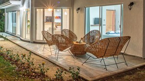 A patio area with wicker furniture and a small table, surrounded by a garden with plants and a tiled floor. - Big family? This is the perfect place, a giant villa close to the beach! (Playa del Carmen)