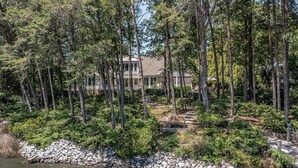 A house surrounded by tall trees and a rocky shoreline. - Waterfront Bay Home, Amazing Water Views, with Private Saltwater Pool (Heathsville)