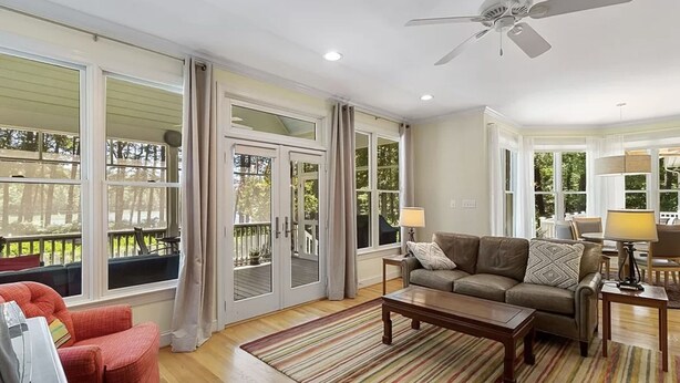 A spacious living room with a large window, a ceiling fan, and a wooden coffee table. - Waterfront Bay Home, Amazing Water Views, with Private Saltwater Pool (Heathsville)
