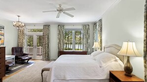 A spacious bedroom with a large bed, a ceiling fan, a chandelier, a desk, and a view of a balcony with curtains. - Waterfront Bay Home, Amazing Water Views, with Private Saltwater Pool (Heathsville)