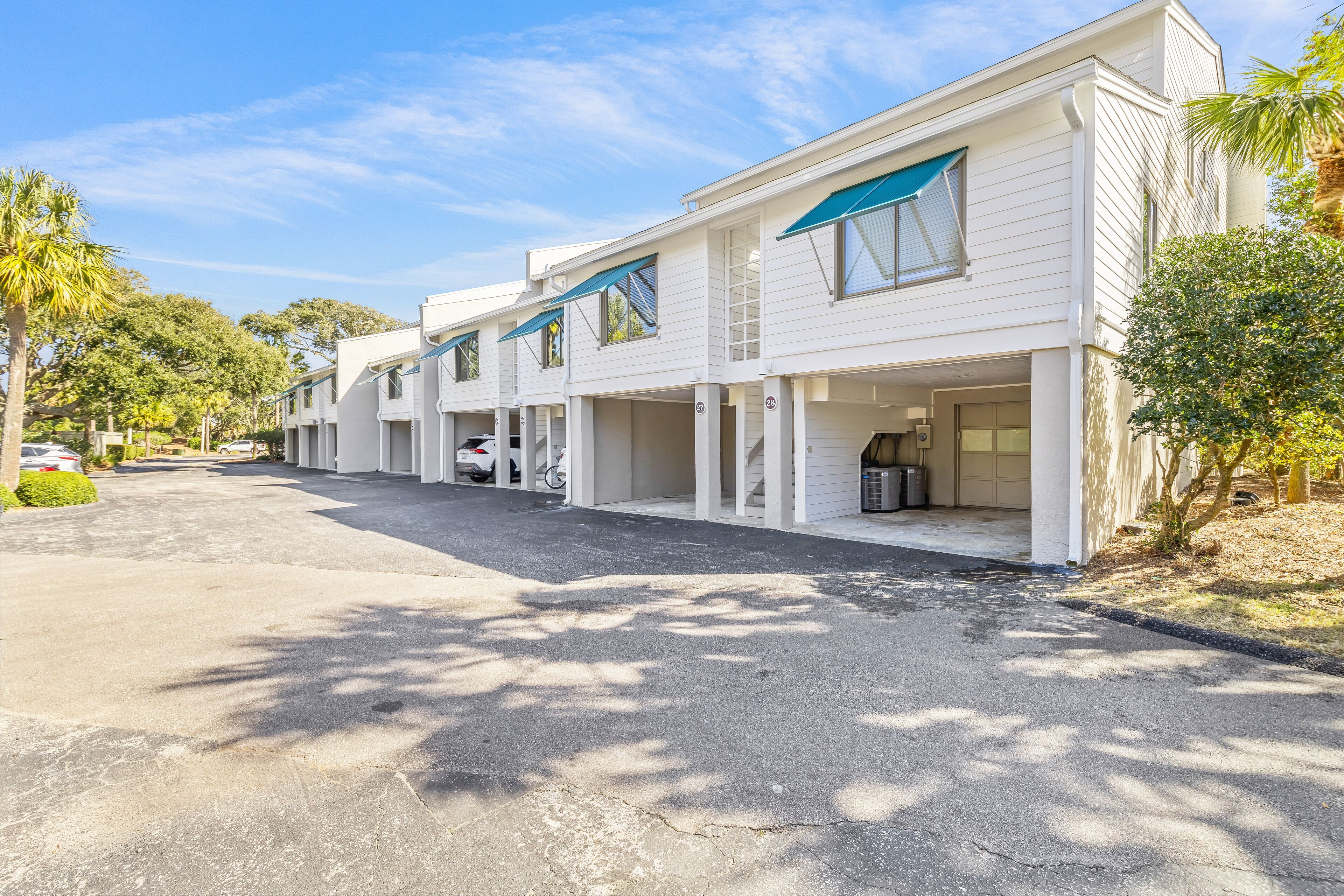 A row of white buildings with blue awnings, a paved driveway, and palm trees.