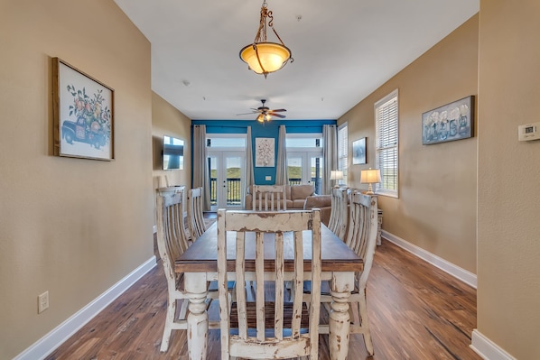 A dining area with a wooden table and chairs, a ceiling fan, and a view of the outdoors through a glass door.